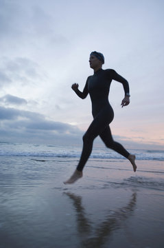 Hispanic woman in wetsuit running on beach