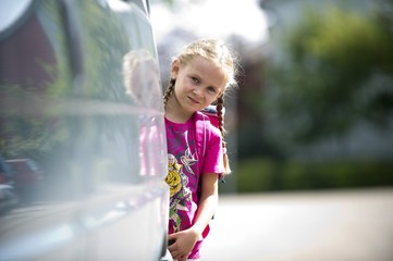 Schülerin blickt hinter einem Auto hervor
