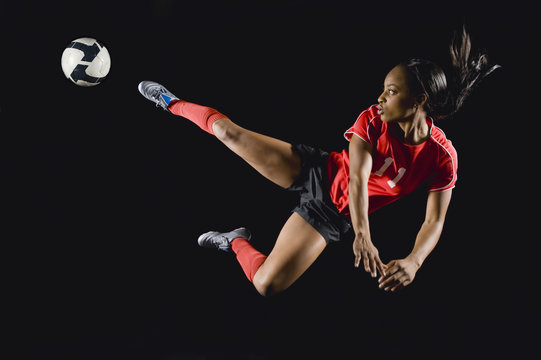 Mixed race soccer player kicking soccer ball in mid-air