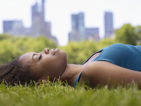 African woman laying on grass in park - Powered by Adobe