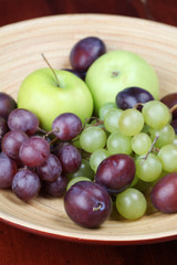Bowl with fresh organic apples, grapes and plums