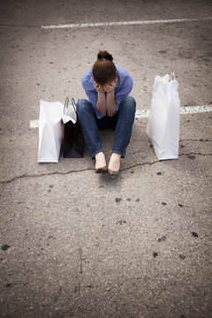 Lost Woman Sitting In Parking Lot With Shopping Bags Covering Fa