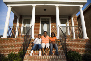 "African mother, daughter and son sitting on front stoop of house"