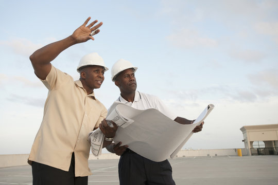 African businessmen looking at blueprints in parking lot