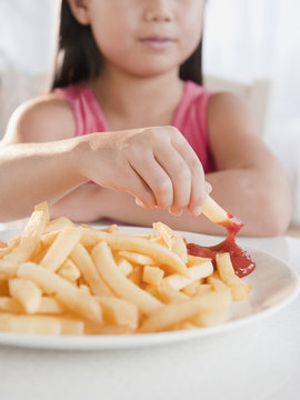 Mixed race girl eating French fries and ketchup