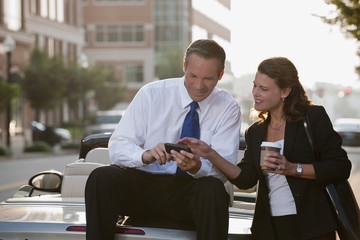 Caucasian businessman sitting on car text messaging with co-worker