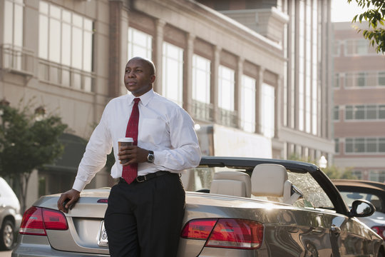 Black businessman drinking coffee near convertible