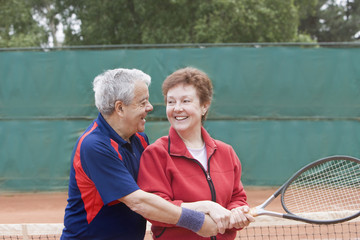 Senior Hispanic man teaching wife to play tennis