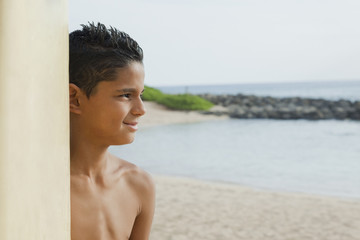 Mixed race boy on beach with surfboard