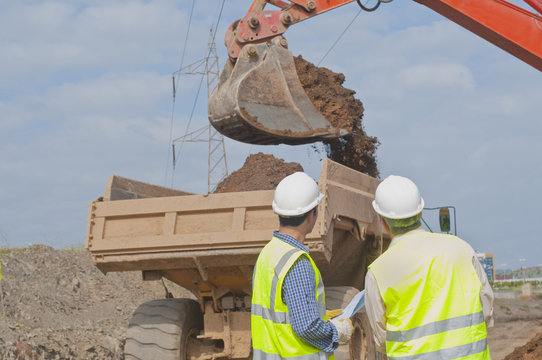 Hispanic construction workers watching dirt falling into dump truck