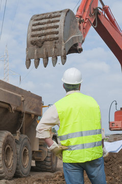 Hispanic construction worker watching backhoe
