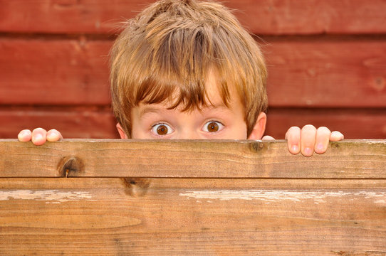 Kind versteckt sich hinter einer Holzwand
