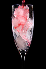 glass full of ice cubes being poured with red drink