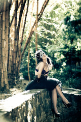 Woman in bra and heels sitting under bamboos