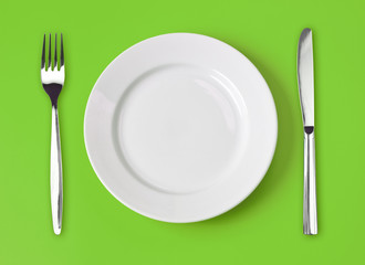 Knife, white plate and fork on green background