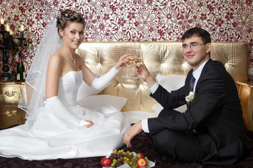 Happy bride and groom making toast on bed