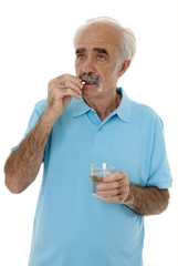 Elderly man swallowing a pill holding a glass of water