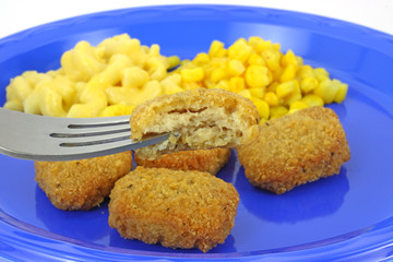 Chicken nugget on fork with meal in background.