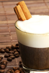 zimtstangen in espresso in kleinem glas mit milchschaum