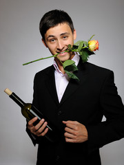Handsome romantic young man holding rose flower and vine bottle