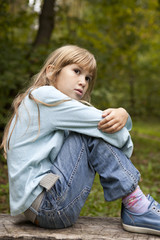 serious little girl nine years old sitting on bench in park