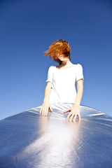 Fototapeta na wymiar Portrait of red-haired girl in white which keep reflector on blu
