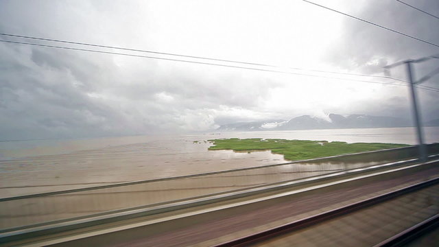 A view of the landscape from moving train passes over lake