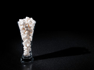 Glass of sugar tubes with long shadow in dark
