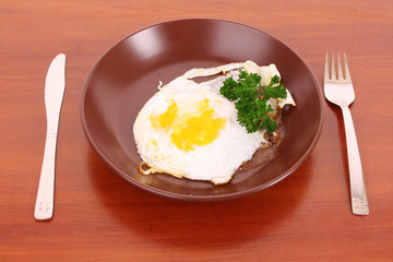 Frying egg with fork and knife on the table