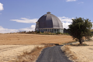A round barn stands on a hill at the end of a lane.