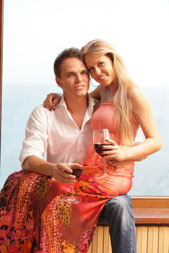 Young couple holding glasses with wine sitting near the window