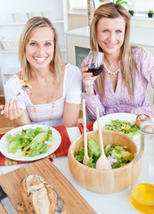 Two positive female friends eating salad in the kitchen