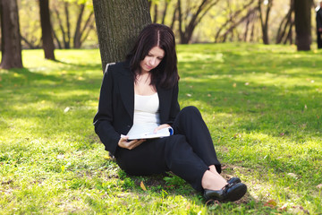 The businesswoman sitting on a grass, reading a book