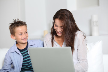 Obraz premium Little boy and mother sitting on sofa at home with laptop