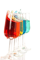 Four different coloured drinks splashing over the edge of glasse