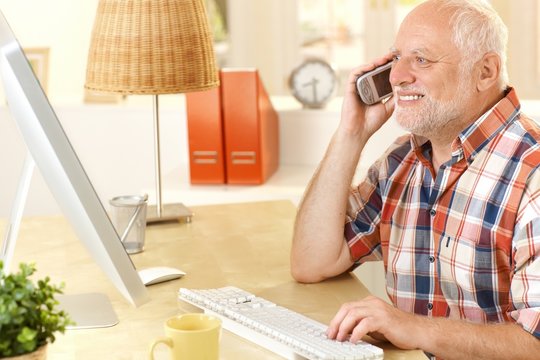 Senior man talking on cellphone, using computer