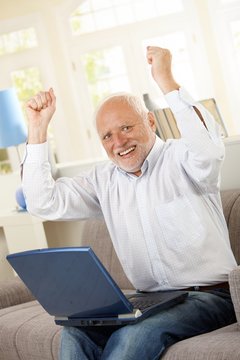 Happy old man sitting on sofa with laptop