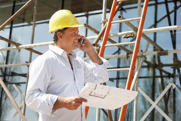 Architect With Plans Outside New Home Talking On Mobile Phone