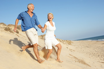 Senior Couple Enjoying Beach Holiday Running Down Dune - Powered by Adobe