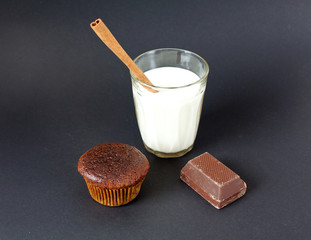 glass of milk, chocolate muffin and cinnamon stick on black