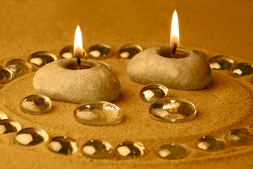 Candles and glass drops on sand. Gold tinted