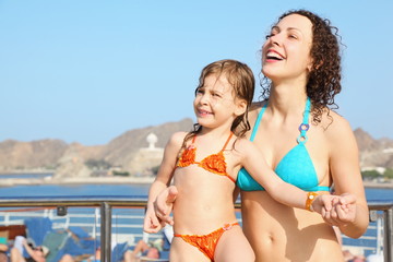 smiling woman with daughter is standing on deck of cruise ship