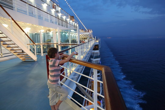 Boy Wearing Shorts And Striped Shirt Standing On Deck Of Ship