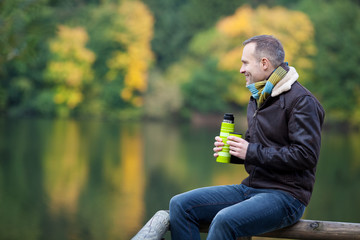 mann mit heißem tee am see