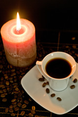 Cup of the fresh coffee and candle on the black background.