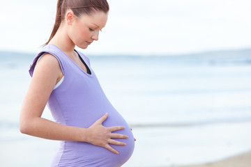 Fototapeta na wymiar Pregnant beautiful woman watchning her stomach on the beach