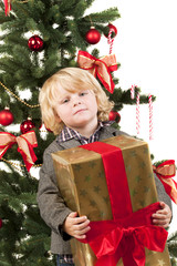 Junge mit Geschenk vor dem Weihnachtsbaum