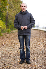 young man with beard standing on path in autumn park, full body