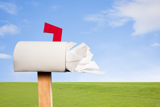 Mail Box Overflowing With Mail Against Sky And Grass