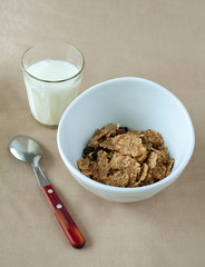 bowl of cornflakes and glass of milk on beige tablecloth